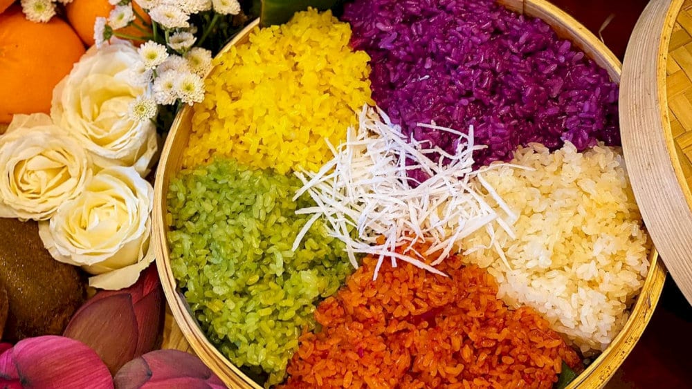 A bamboo tray of colorful sticky rice arranged like a rainbow, usually served with sesame salt